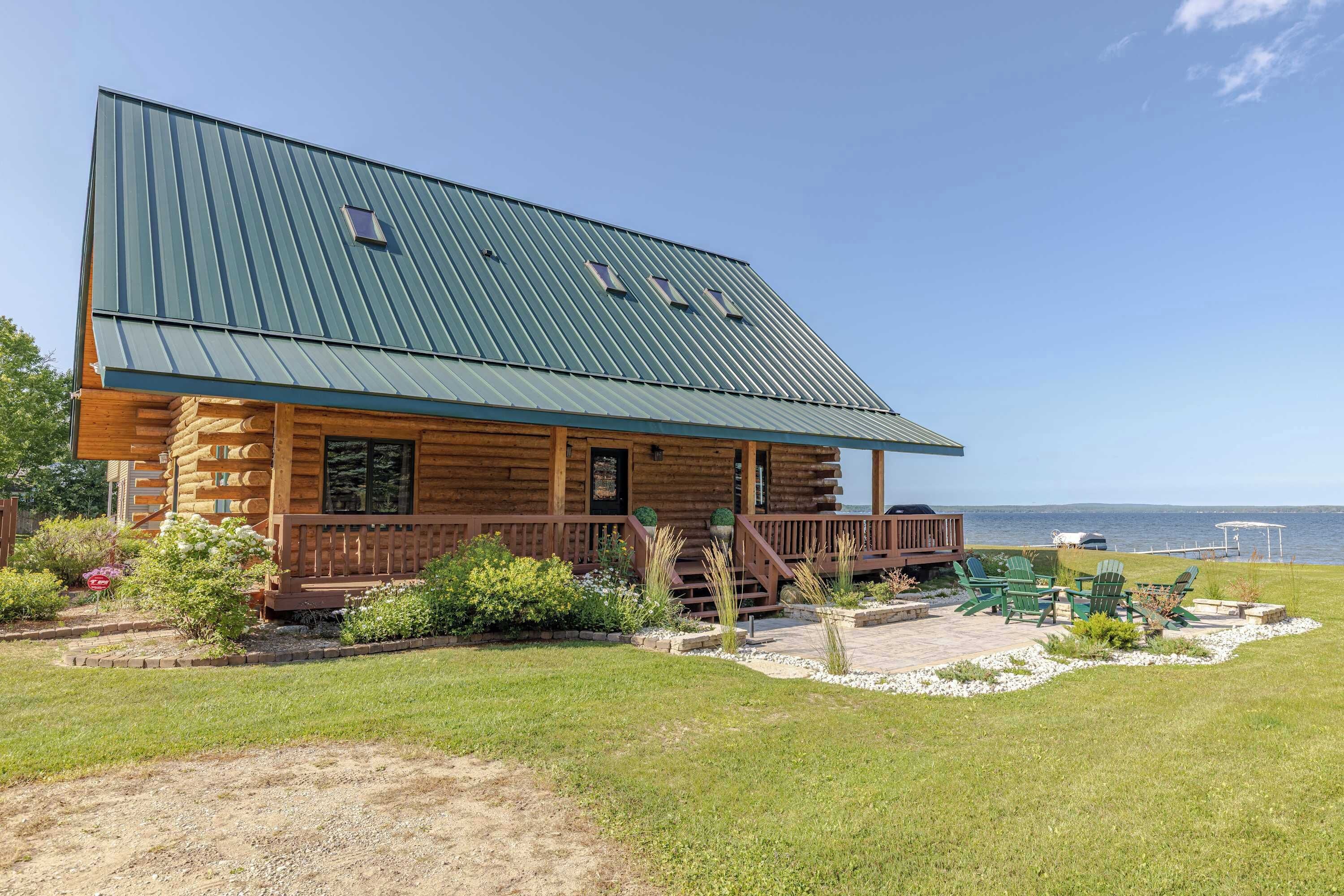 A log cabin with a metal roof, a porch, and a view of the water.