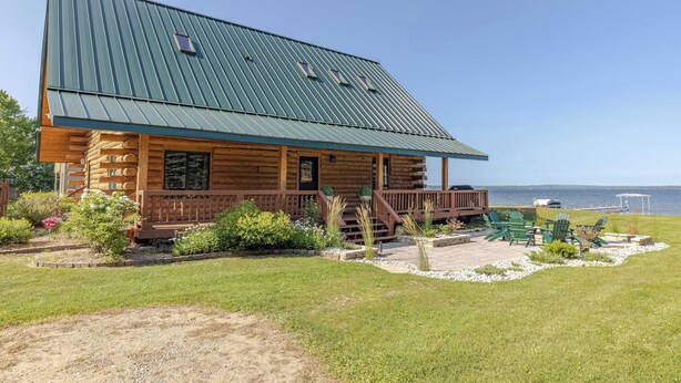 Une cabane en rondins avec un toit en métal, une véranda et une vue sur l’eau.