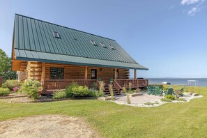 A log cabin with a metal roof, a porch, and a view of the water.