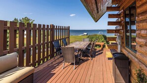 Une terrasse en bois avec une table et des chaises, donnant sur une étendue d’eau.