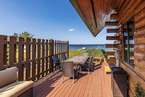 A wooden deck with a table and chairs, overlooking a body of water. - Lakefront Log Cabin | Private Dock, Beach, Firepit (Curtis)