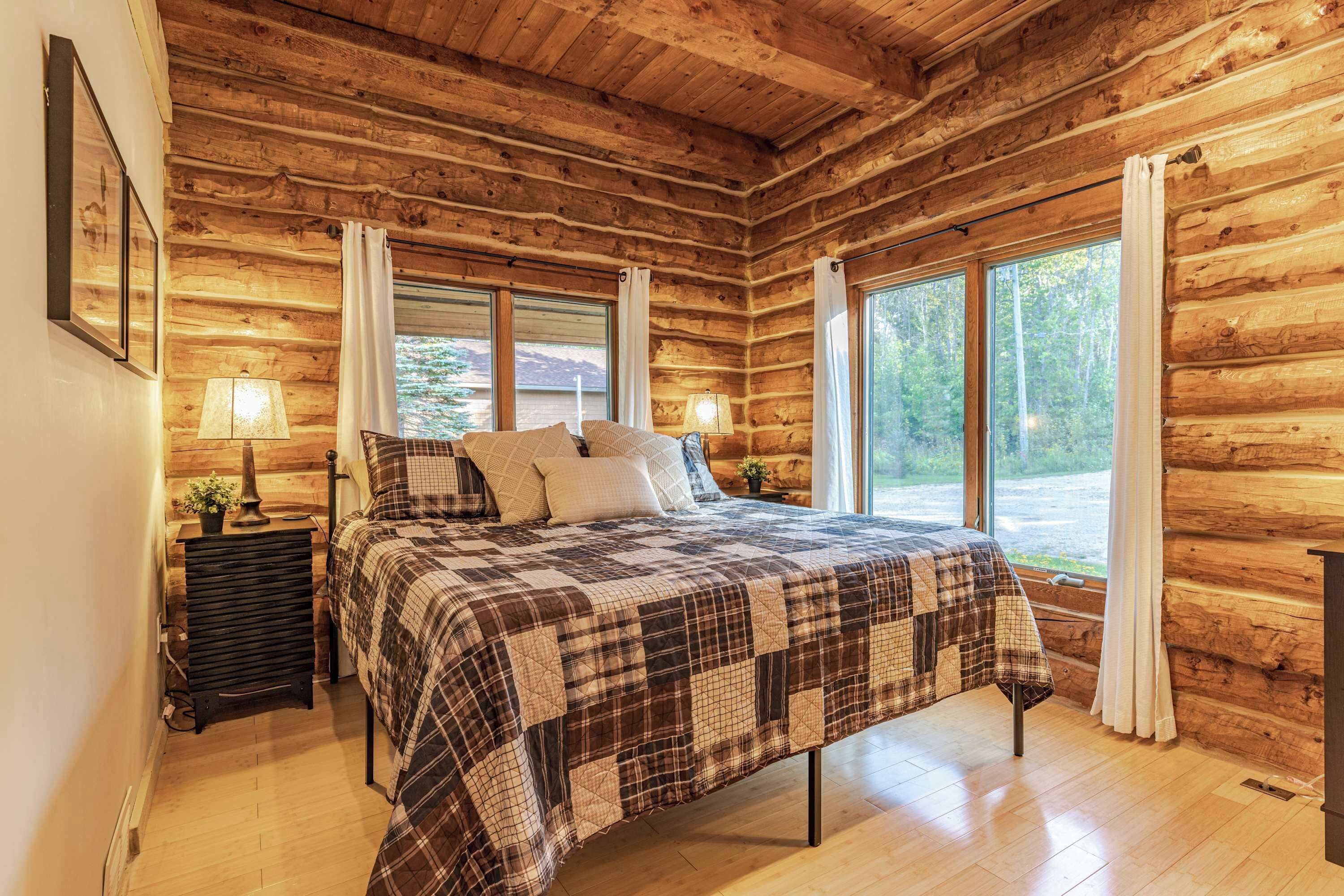 A log cabin bedroom with a bed, two bedside lamps, and large windows.