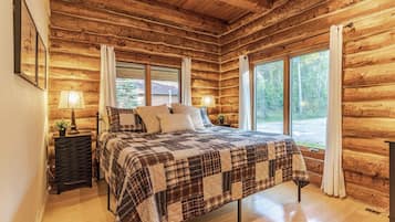 A log cabin bedroom with a bed, two bedside lamps, and large windows.