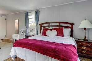 A bedroom with a bed, bedside tables, a lamp, a fan, and a window with curtains.