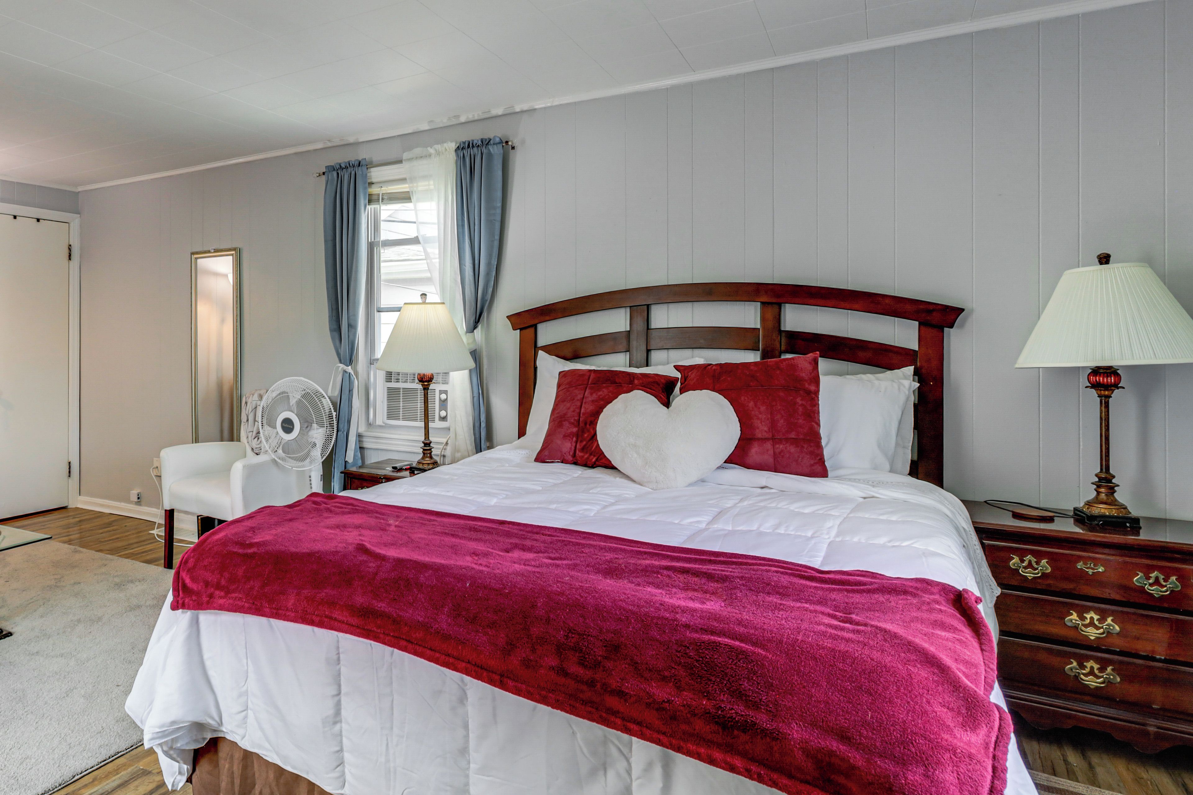 Une chambre à coucher avec un lit, des tables de chevet, une lampe, un ventilateur et une fenêtre avec des rideaux.