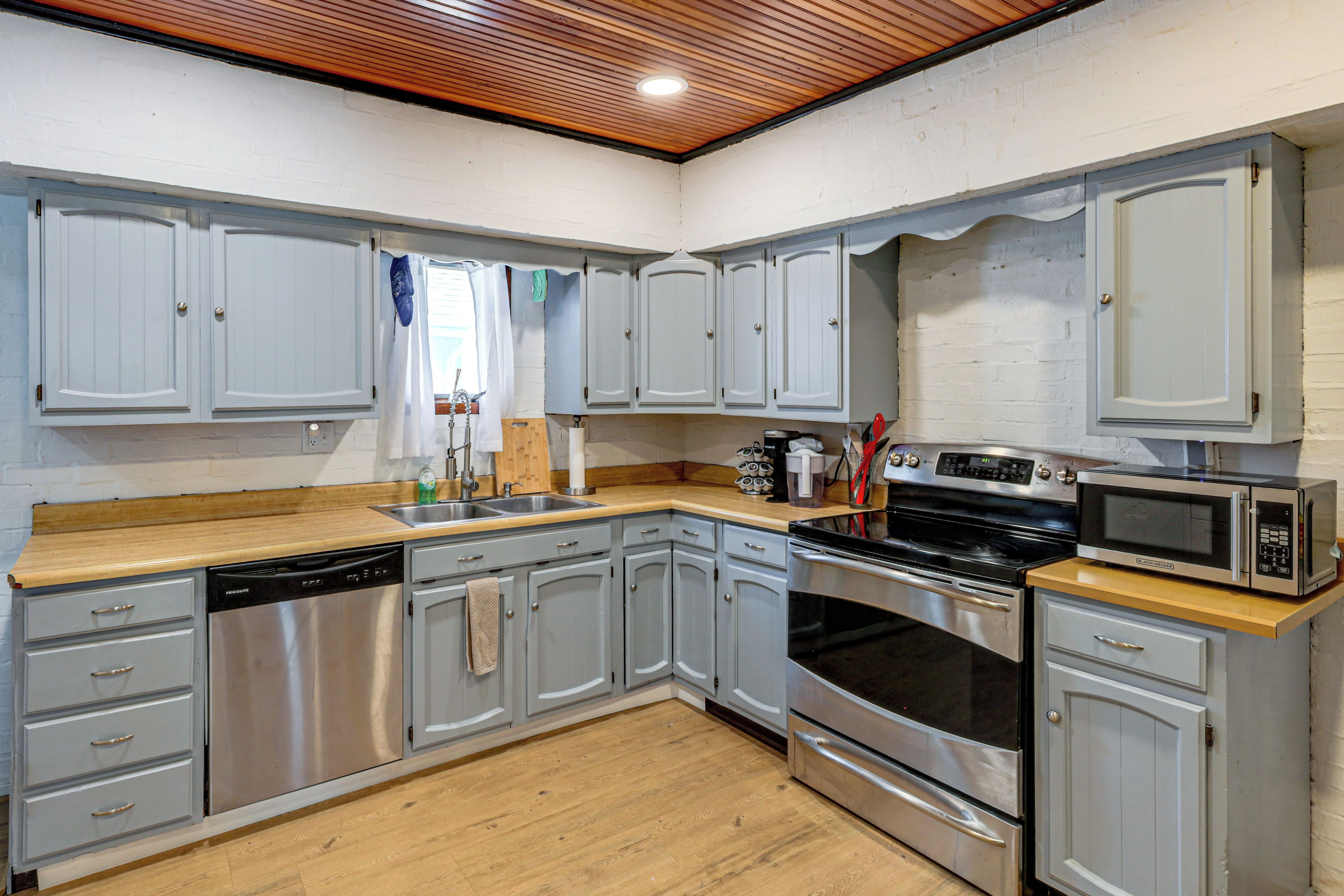 A kitchen with grey cabinets, a wooden countertop, a dishwasher, an oven, and a microwave.