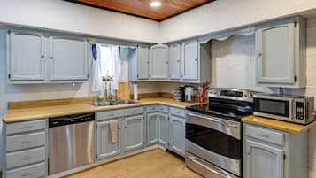 A kitchen with grey cabinets, a wooden countertop, a dishwasher, an oven, and a microwave.