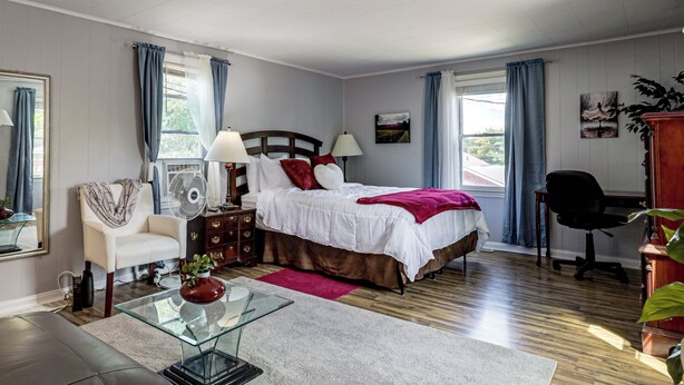 Ein Schlafzimmer mit Bett, Nachttischen, einem Sessel, einem Schreibtisch und einem Fenster mit Vorhängen.