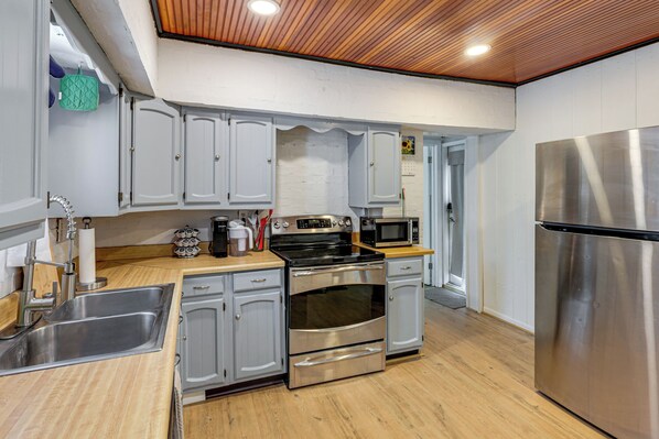 A modern kitchen with stainless steel appliances, wooden flooring, and white cabinetry.