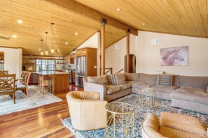 A spacious living area with a large sofa, a coffee table, and a rug. There is a kitchen in the background with wooden cabinets and a refrigerator. - Dock + Hot Tub! Waterfront Lake Tahoe Getaway (South Lake Tahoe)