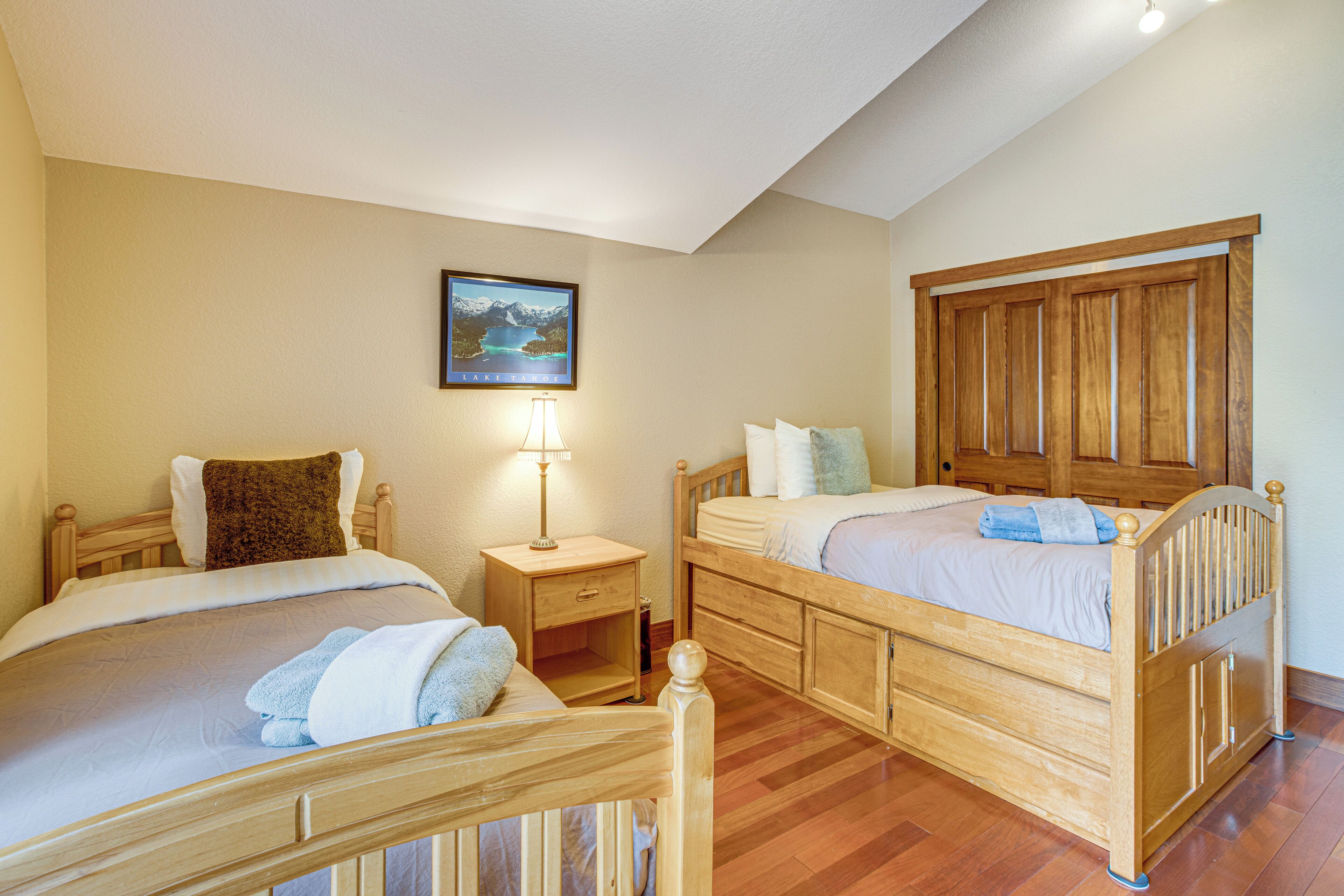 Quarto com duas camas de madeira, uma mesa de cabeceira, um abajur e um quadro pendurado na parede.