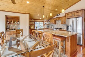 A spacious kitchen with wooden cabinetry, a stainless steel refrigerator, and a glass-top dining table with chairs. - Dock + Hot Tub! Waterfront Lake Tahoe Getaway (South Lake Tahoe)