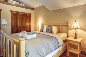 Un dormitorio con cama, cabecera de madera, mesitas de noche y un velador.