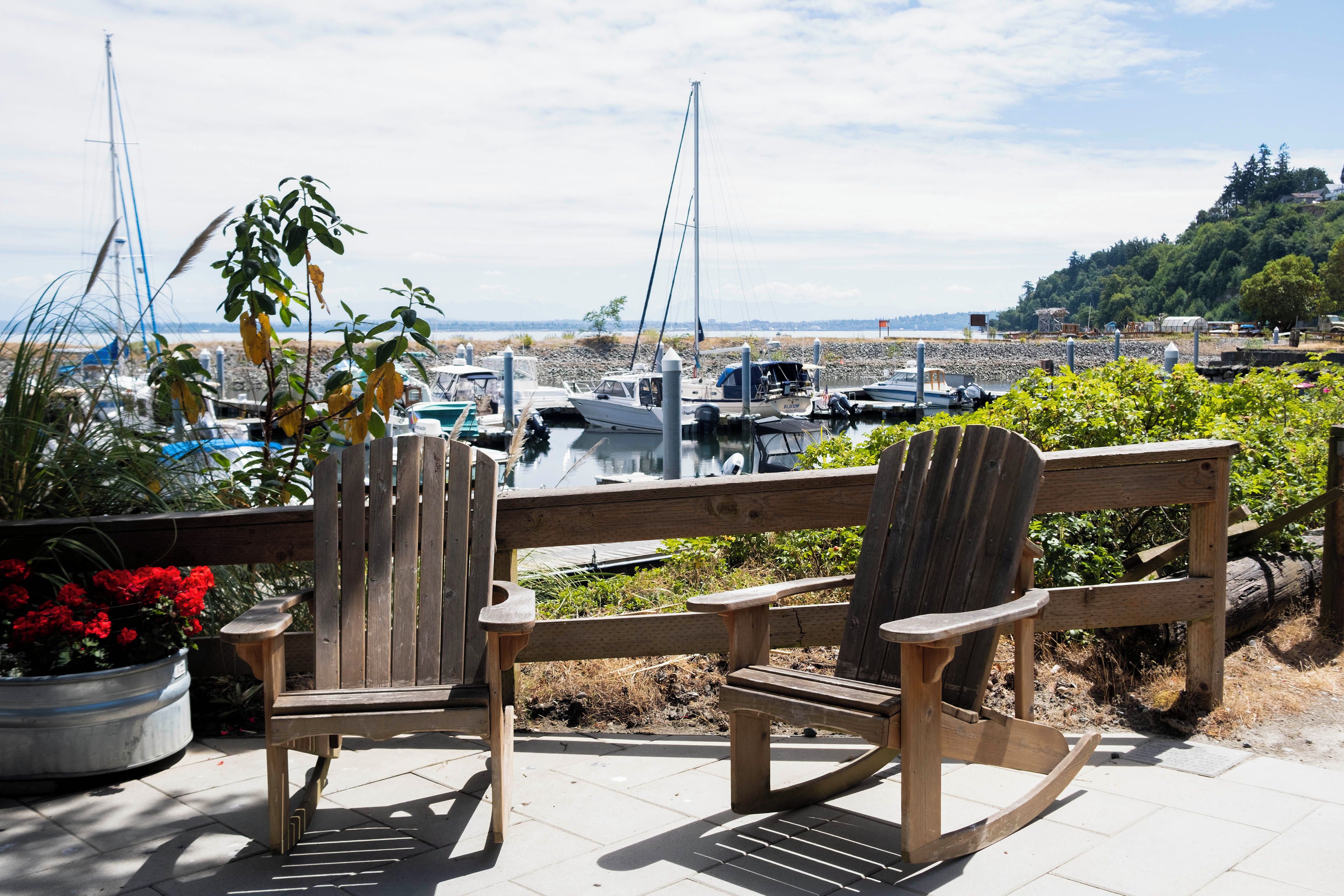 Eine Holzterrasse mit Adirondack-Stühlen mit Blick auf eine Marina und Boote.