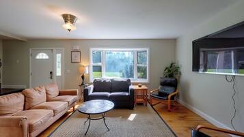 Un salon comprenant un canapé, une table basse et un fauteuil. Une fenêtre offre une vue sur la verdure environnante.