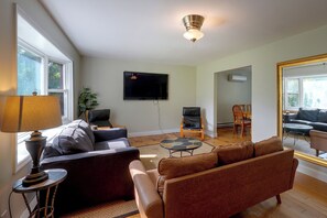 A living room with a sofa, a coffee table, a TV mounted on the wall, and a ceiling fan.