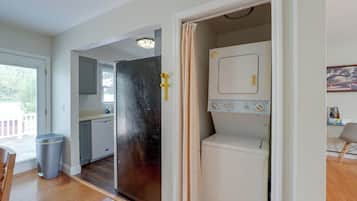 A compact kitchen with a dishwasher, a small refrigerator, and a window with blinds.