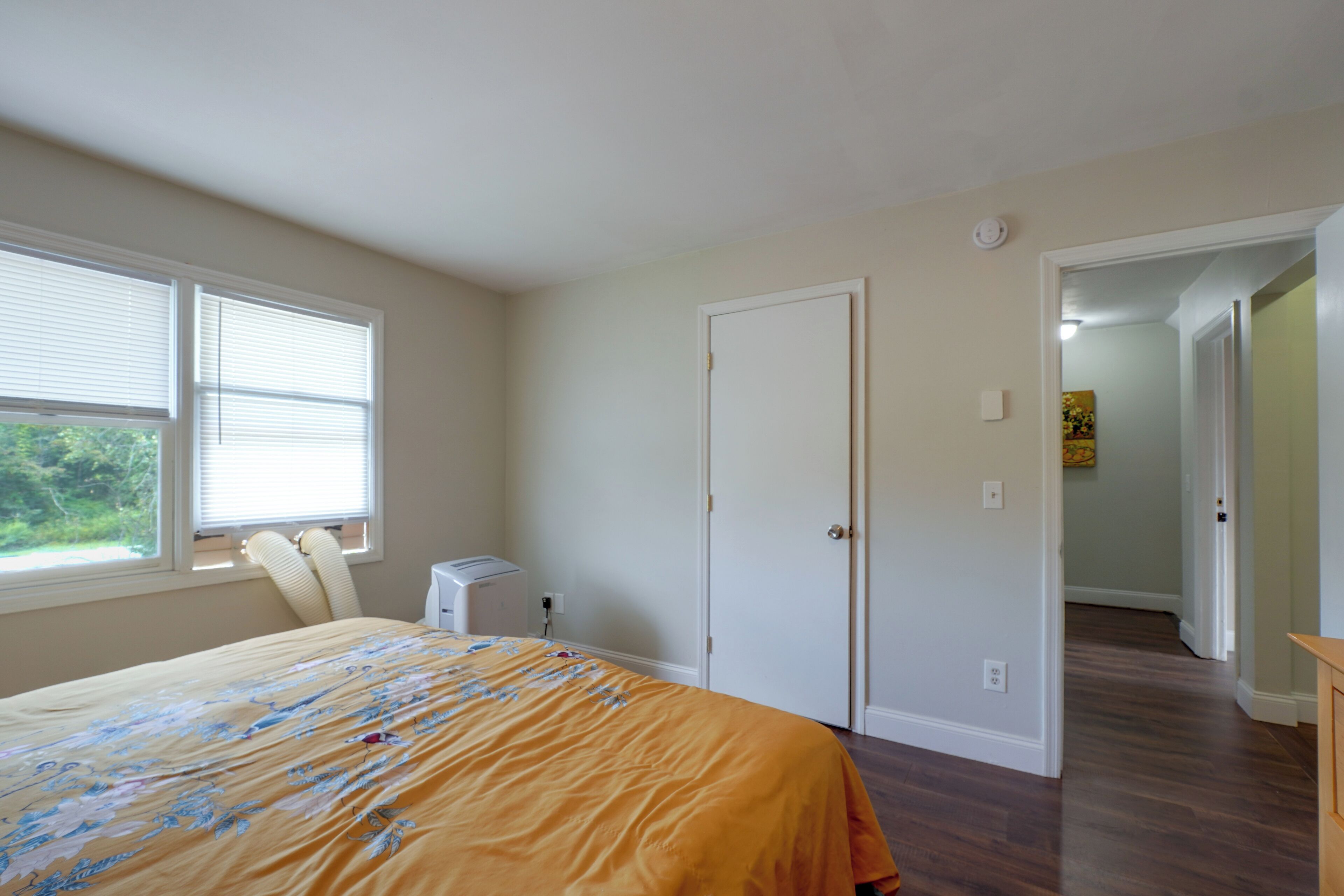 A bedroom with a bed, a window, a heater, and a door leading to another room.
