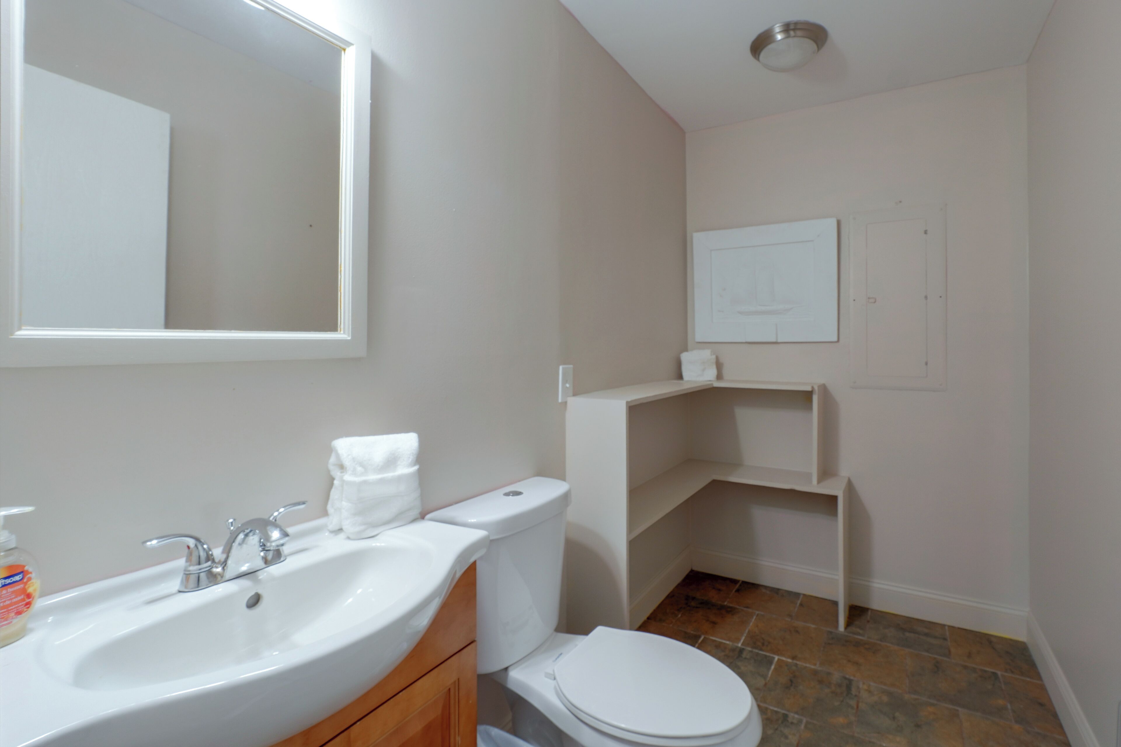 A bathroom with a white sink, toilet, and a mirror. There is a towel on the toilet and a soap dispenser on the sink.