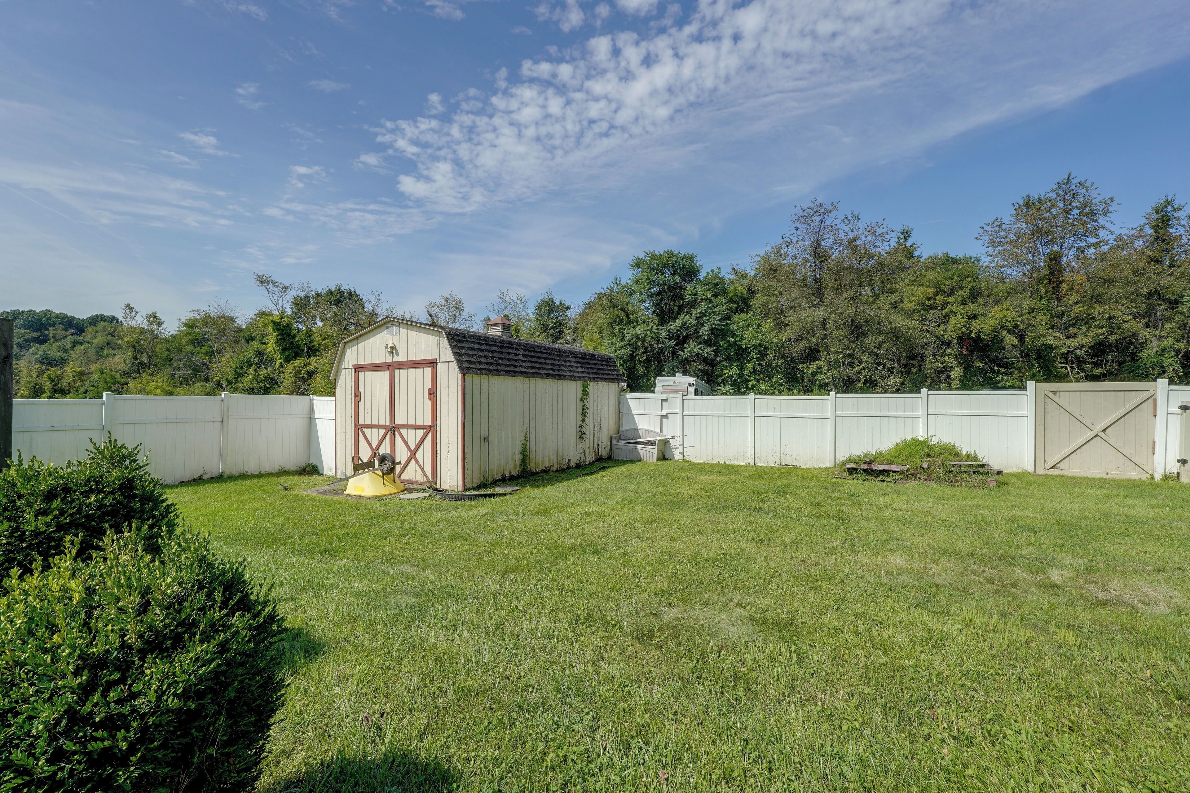 A fenced backyard with a small shed, a lawn mower, and a white fence.