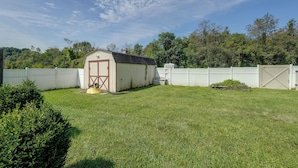 A fenced backyard with a small shed, a lawn mower, and a white fence. - Hudson Valley Duplex: Hike, Sip + Explore! (Highland)