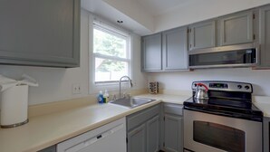 A compact kitchen with a dishwasher, a stove, a microwave, and a window with blinds. - Hudson Valley Duplex: Hike, Sip + Explore! (Highland)