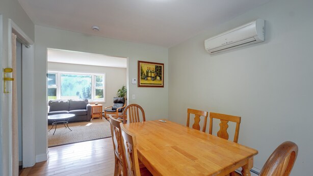 A dining area with a wooden table and chairs, a living room with a sofa and a window, and an air conditioning unit on the wall. - Hudson Valley Duplex: Hike, Sip + Explore! (Highland)