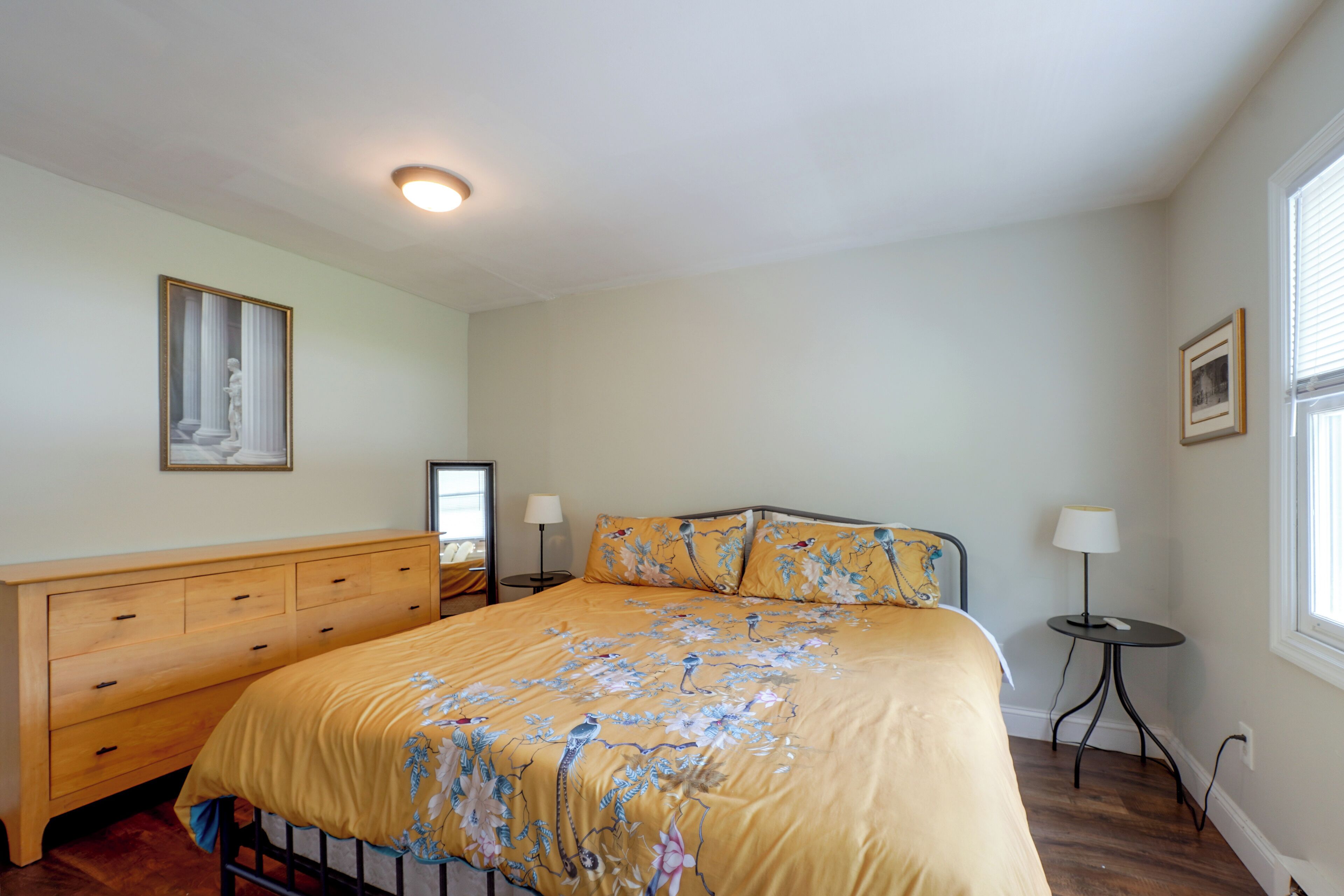 A bedroom with a bed, bedside tables, a dresser, a window, and a ceiling light.