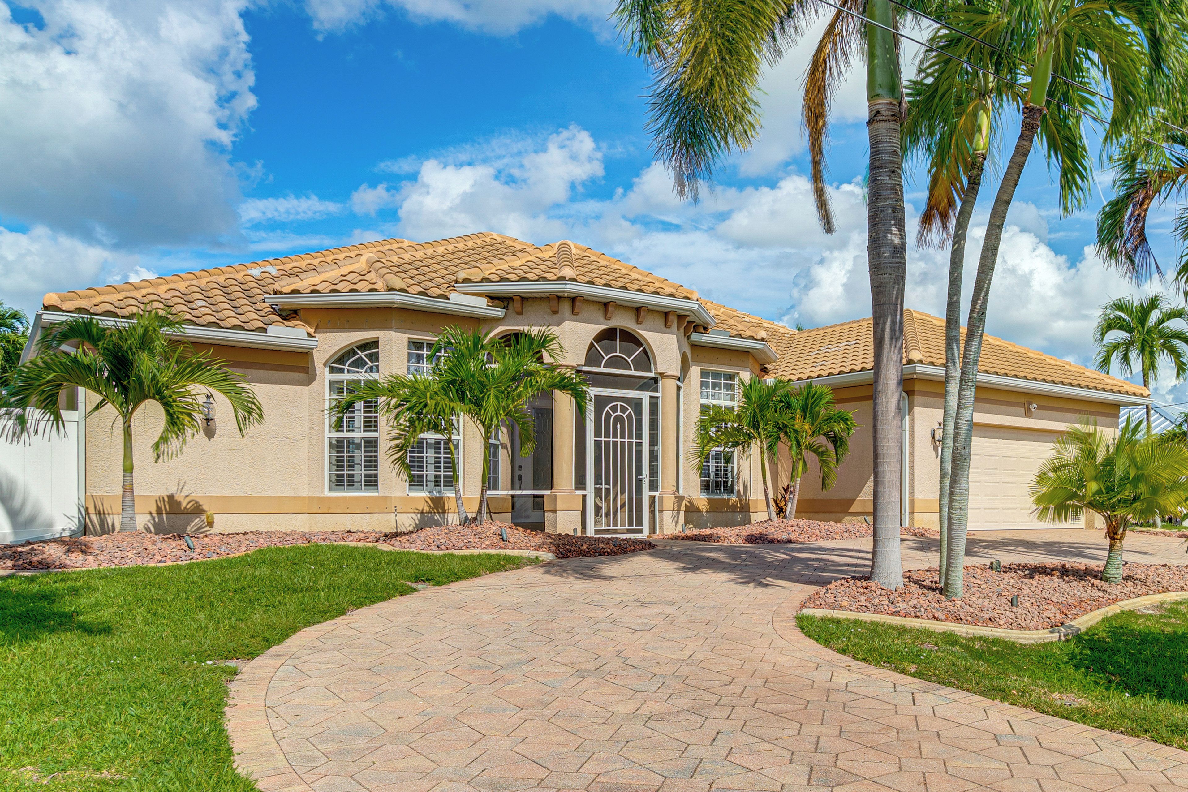 A two-story house with a tiled roof, a front entrance with a glass door, and palm trees in the yard.