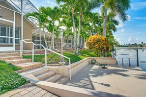 A residential property with a staircase leading to a covered porch, surrounded by palm trees and a body of water. - Great for Groups! Canalfront Cape Coral Getaway (Cape Coral)