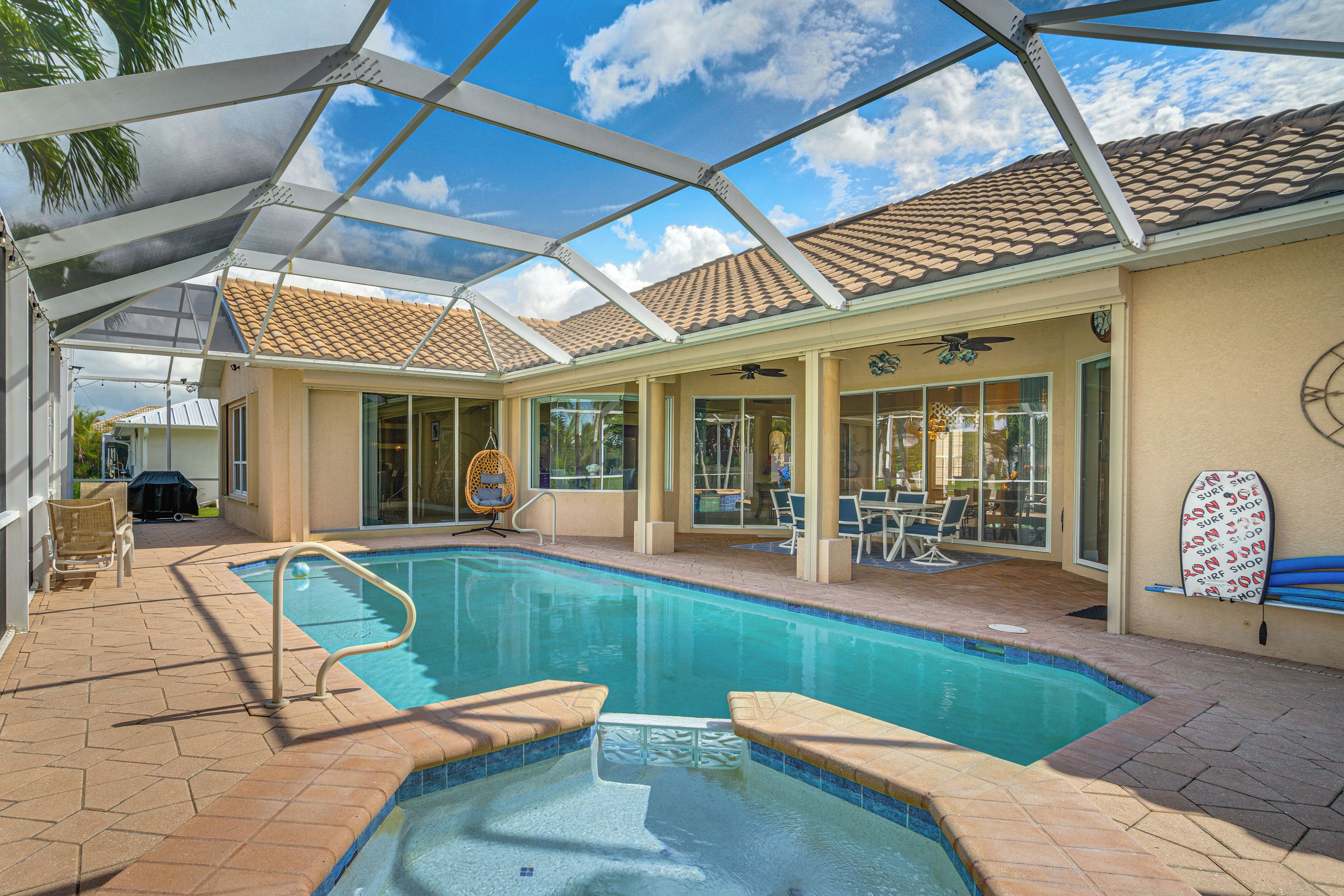 A covered outdoor swimming pool with a patio area, a ceiling fan, and a surfboard decoration.