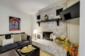 A living room with a fireplace, a sofa, a coffee table, and a wall-mounted TV. - Easy Raleigh Access! Quaint Apt w/ Patio (Garner)