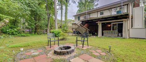 A backyard with a fire pit, two chairs, a wooden deck, and a brick building.