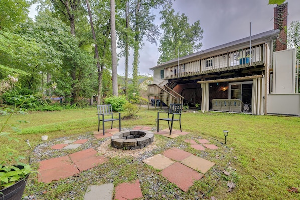 A backyard with a fire pit, two chairs, a wooden deck, and a brick building. - Easy Raleigh Access! Quaint Apt w/ Patio (Garner)