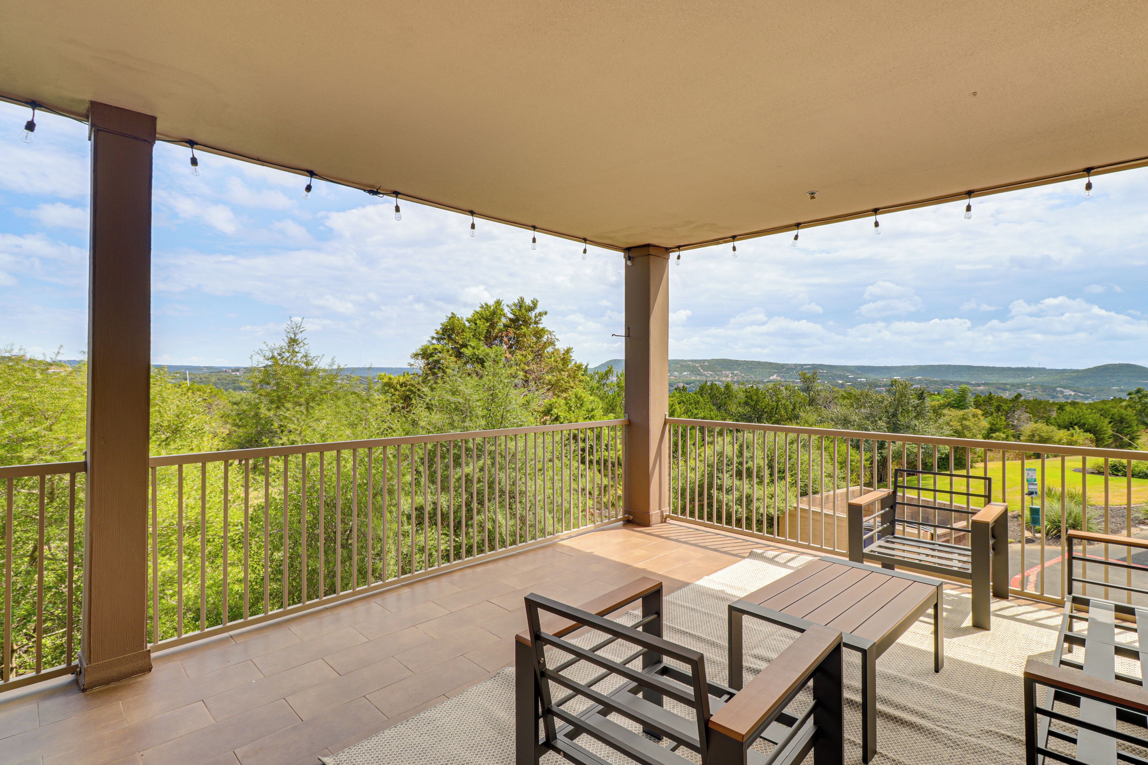 A covered outdoor area with a view of a green landscape, a table, and chairs.