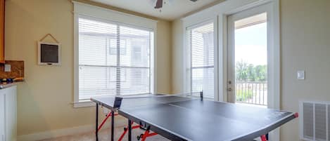 Une pièce avec une table de ping-pong, un ventilateur de plafond et une vue par les fenêtres.