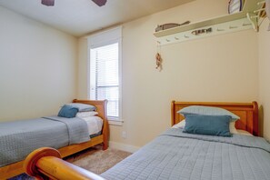 A bedroom with two single beds, a wooden headboard, a window with blinds, and a wall-mounted shelf with various items. - Lake Travis Escape at The Hollows (Leander)