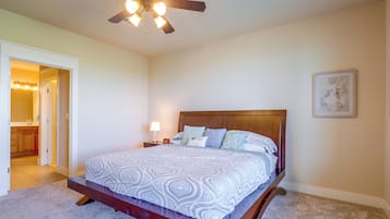 Quarto com cama, mesa de cabeceira, relógio na parede, ventilador de teto e porta que dá para um banheiro.