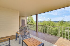 A balcony with a view of greenery and hills, a wooden table, and a seating area with chairs. - Lake Travis Escape at The Hollows (Leander)