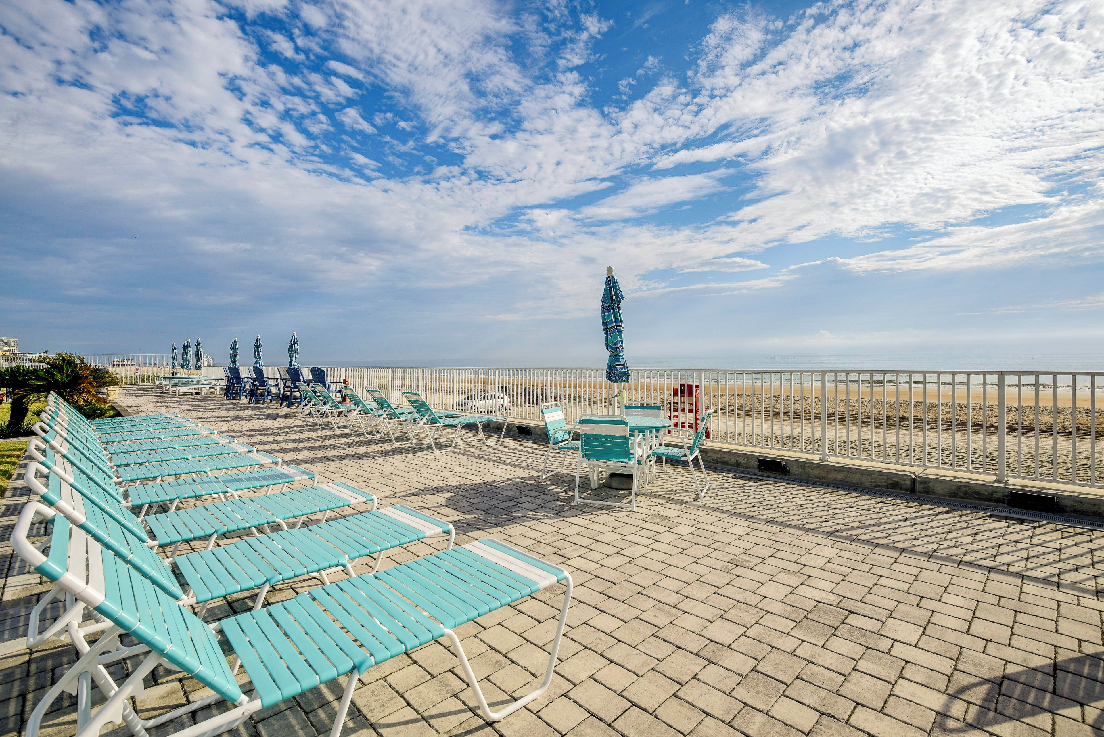 Eine Terrasse direkt am Strand mit Reihen von blauen Liegestühlen und einigen Tischen, mit Blick auf den Strand.
