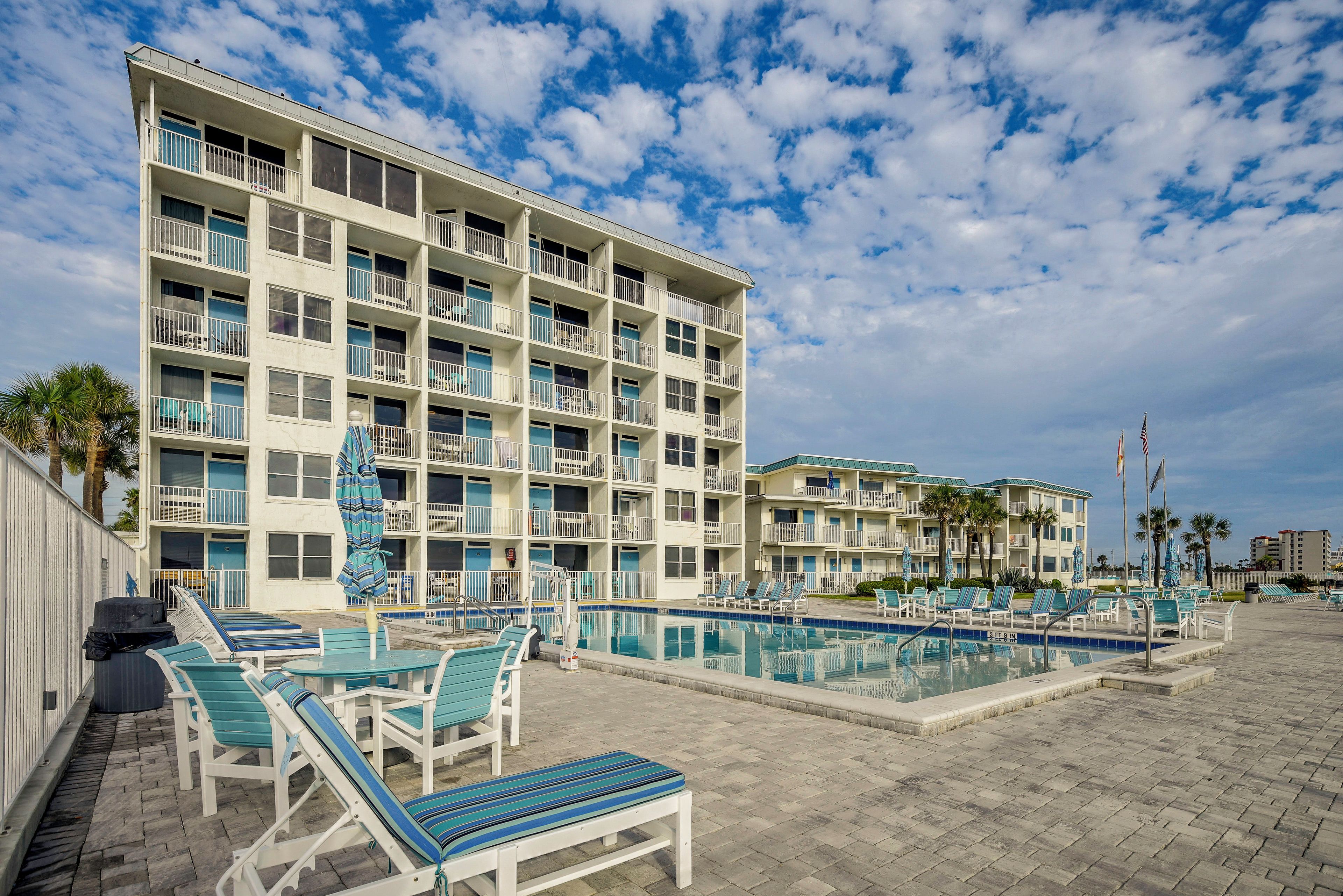 A multi-story hotel with a pool area, including lounge chairs and umbrellas.
