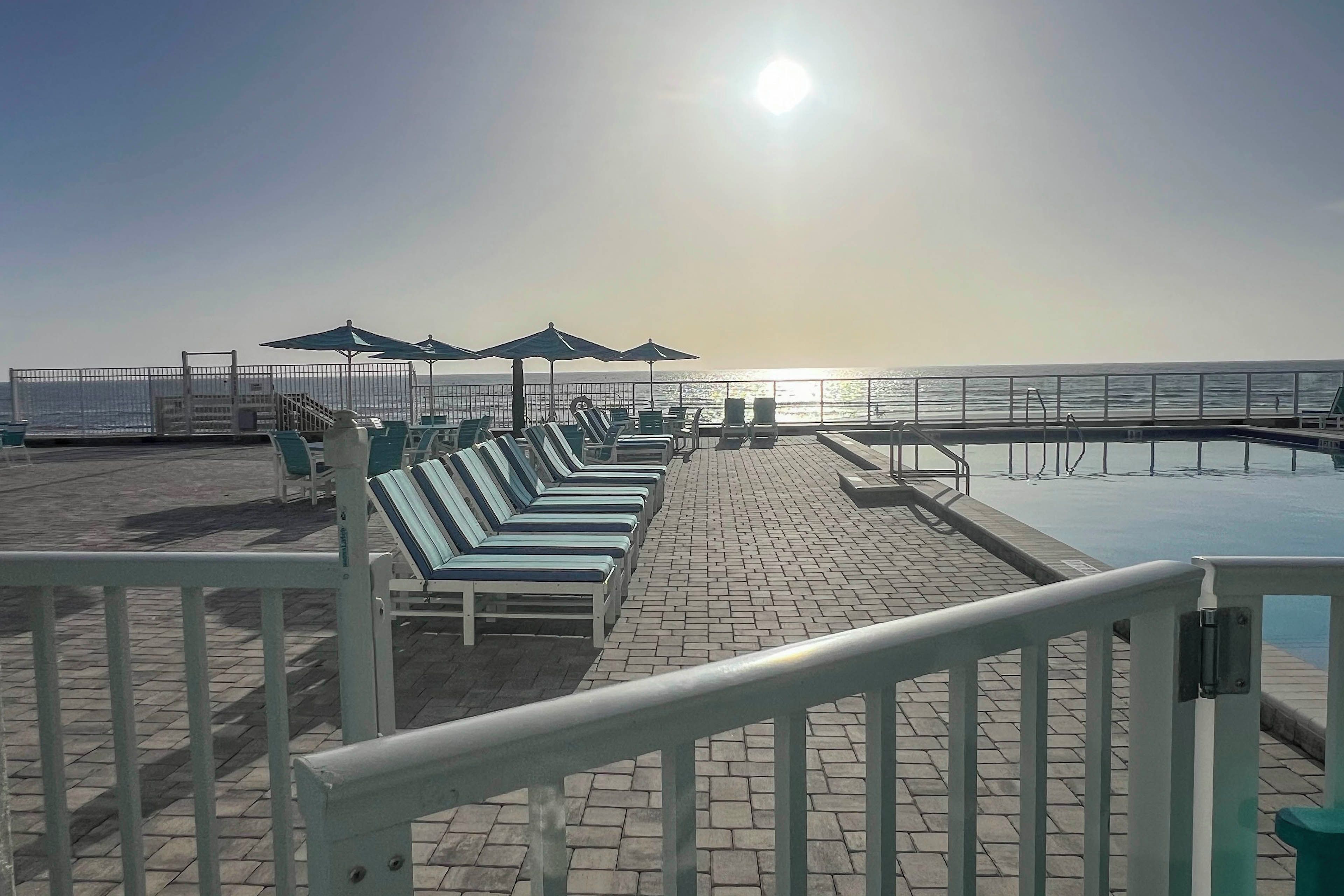 Un espace extérieur ensoleillé, aménagé avec des chaises longues et des parasols, offrant une vue sur une étendue d’eau calme.