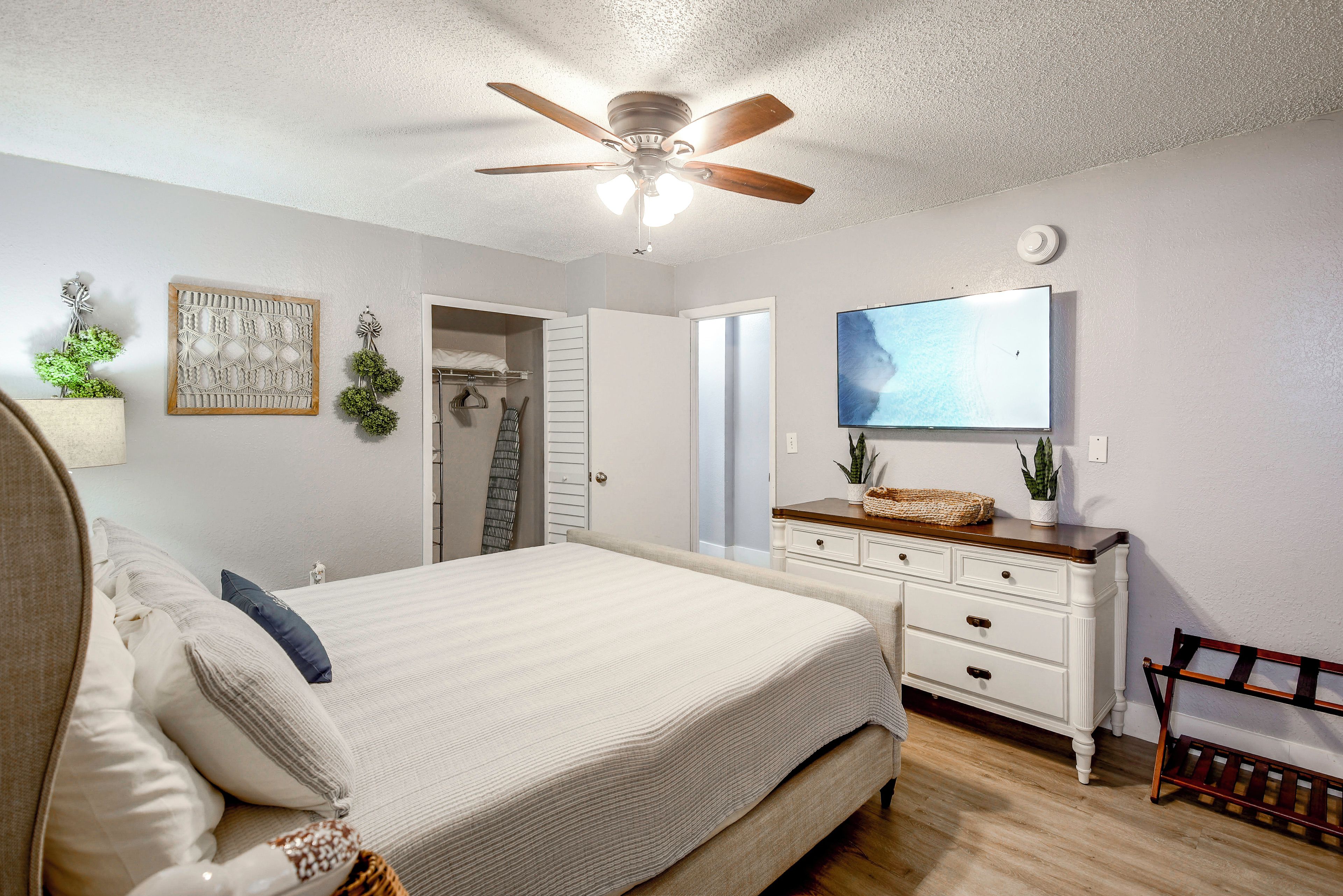 A bedroom with a bed, a dresser, a television, and a ceiling fan.