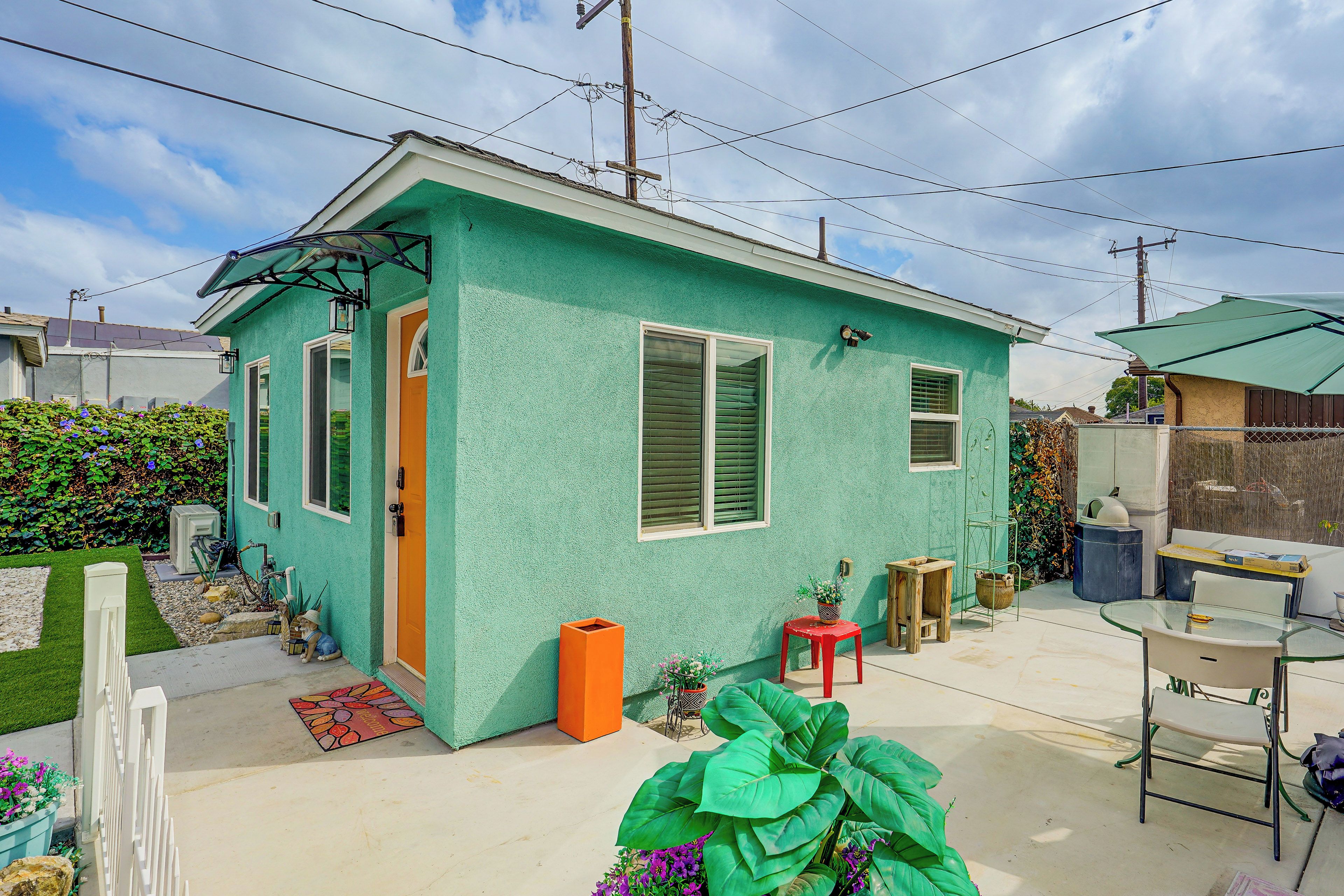 A small house with a green exterior, a door, windows, and a small porch area with a table and chairs.