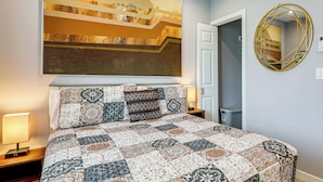A bedroom with a large bed, a wall-mounted mirror, and a painting.