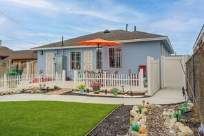 A residential house with a white picket fence, a front porch with outdoor seating, and a well-maintained garden. - Spacious, Cozy Rear House Near LAX (Compton)