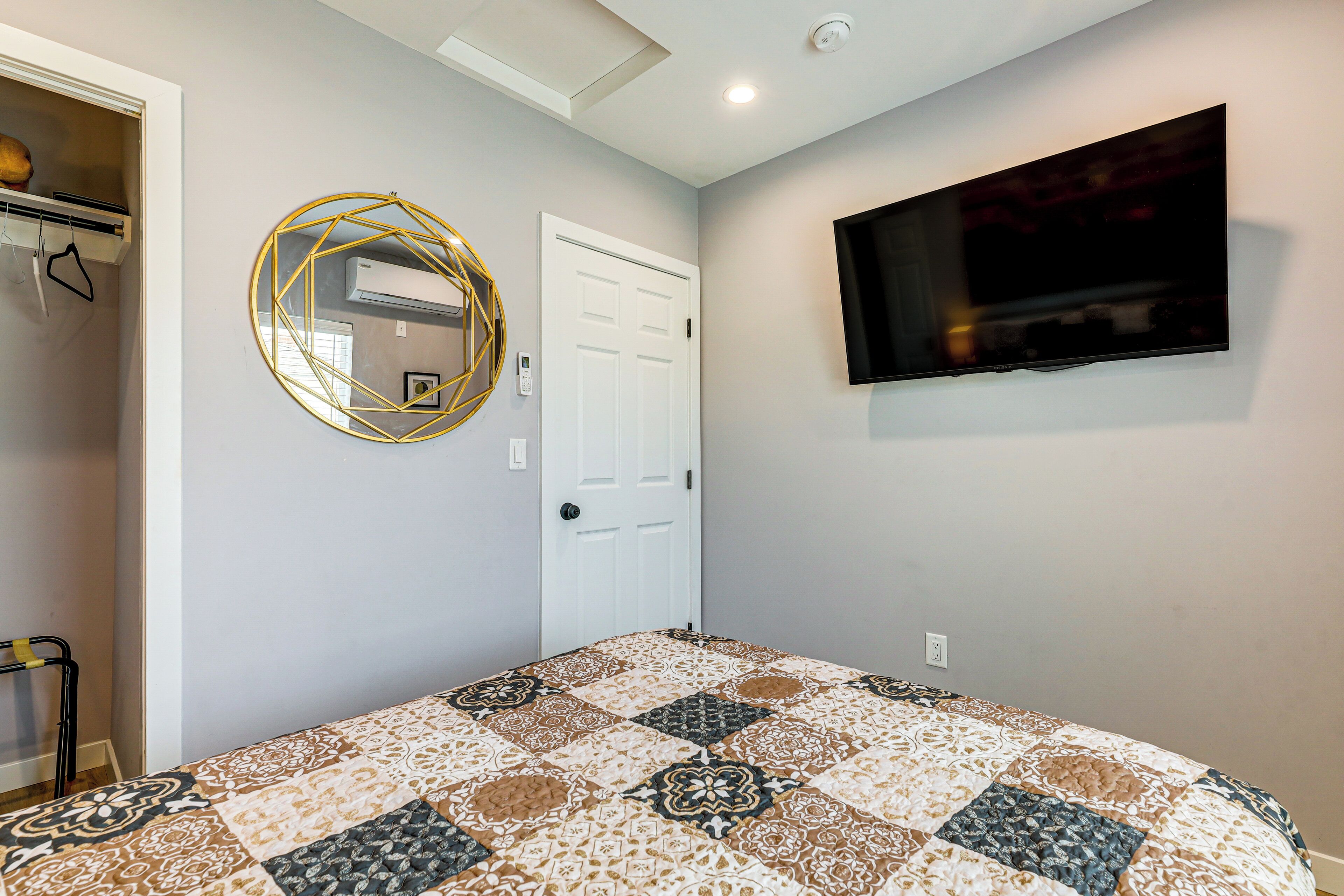 A bedroom with a bed, a television mounted on the wall, a door, and a wall-mounted air conditioning unit.