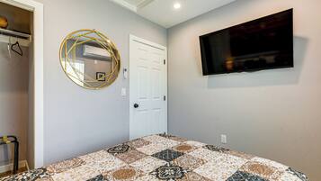 A bedroom with a bed, a television mounted on the wall, a door, and a wall-mounted air conditioning unit.