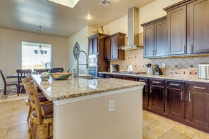 A kitchen with granite countertops, dark wooden cabinets, a built-in oven, and a large island with bar stools. - Las Cruces Oasis: Patio, Hot Tub + Mtn Views (Las Cruces)