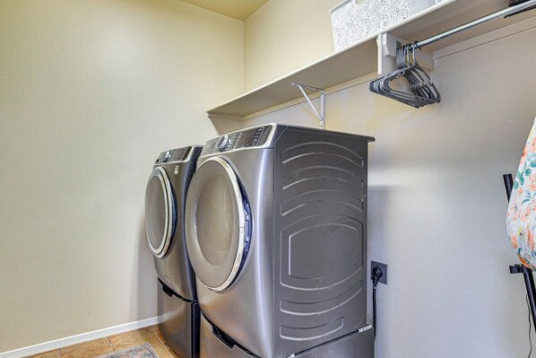 A laundry area with two front-loading washing machines, a metal drying rack, and a small shelf above the machines. - Las Cruces Oasis: Patio, Hot Tub + Mtn Views (Las Cruces)